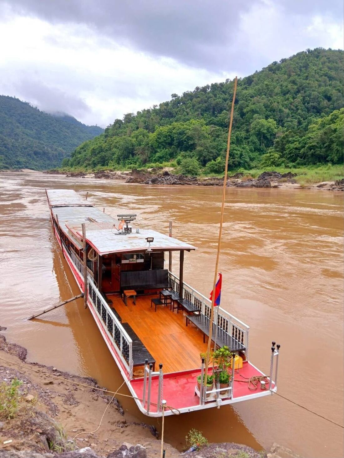 Traditional Mekong slow boat moored by jungle hills